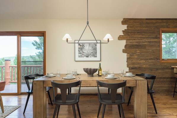 A dining area with a wooden table set for four, chairs, a hanging light fixture, and a framed picture on the wall.