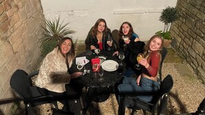 Un grupo de personas sentadas alrededor de una mesa con bebidas, en un ambiente con paredes de piedra y plantas en macetas.