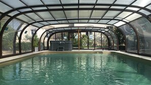 Una piscina interior amb sostre de vidre, envoltada per una estructura metàl·lica, i una zona de seients amb una font.