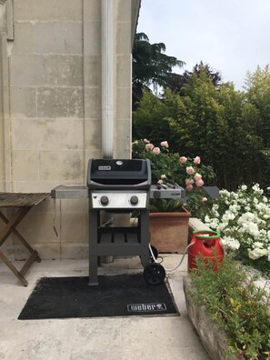 A Weber gas grill outdoors with a black mat labeled 'Weber' in front, a potted plant, and a red container nearby. - 5-star villa with a large pool, hot tub, and sauna in the Loire Valley (Montrichard Val de Cher)