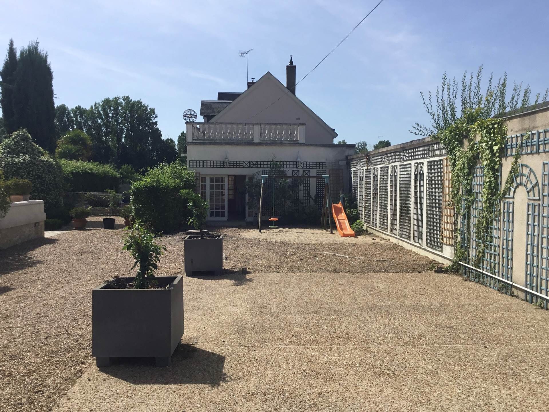 A building with a triangular roof, a fenced area with a slide, and potted plants.
