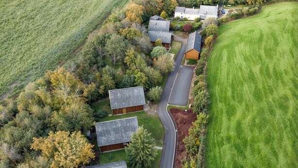 An aerial view of a rural area with houses, a road, and surrounding fields. - Two-bedroom cottage for up to four guests, with Wi-Fi, Netflix-ready TV, private decking, Ninja BBQ, hot tub, EV charging and space for up to three dogs. (Cornwall)