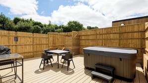 A wooden deck with a hot tub, a table with chairs, and a grill. - Two-bedroom cottage for up to four guests, with Wi-Fi, Netflix-ready TV, private decking, Ninja BBQ, hot tub, EV charging and space for up to three dogs. (Cornwall)