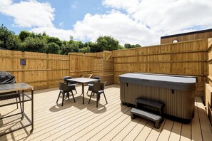 A wooden deck with a hot tub, a table with chairs, and a grill. - Two-bedroom cottage for up to four guests, with Wi-Fi, Netflix-ready TV, private decking, Ninja BBQ, hot tub, EV charging and space for up to three dogs. (Cornwall)