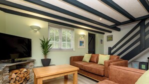 A living room with a TV, a sofa, a coffee table, a fireplace, and a staircase. - Two-bedroom cottage for up to four guests, with Wi-Fi, Netflix-ready TV, private decking, Ninja BBQ, hot tub, EV charging and space for up to three dogs. (Cornwall)