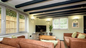 A living room with a stone fireplace, a television, and a potted plant. - Two-bedroom cottage for up to four guests, with Wi-Fi, Netflix-ready TV, private decking, Ninja BBQ, hot tub, EV charging and space for up to three dogs. (Cornwall)