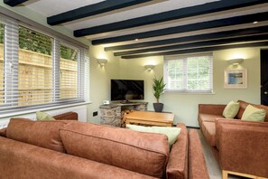 A living room with a stone fireplace, a television, and a potted plant. - Two-bedroom cottage for up to four guests, with Wi-Fi, Netflix-ready TV, private decking, Ninja BBQ, hot tub, EV charging and space for up to three dogs. (Cornwall)