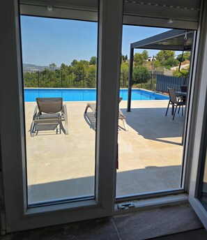 A view through a window of a pool area with lounge chairs and a pergola. - 3 Bed, 2 Bath Villa with private pool in quiet location 45mins to Valencia (Catadau)