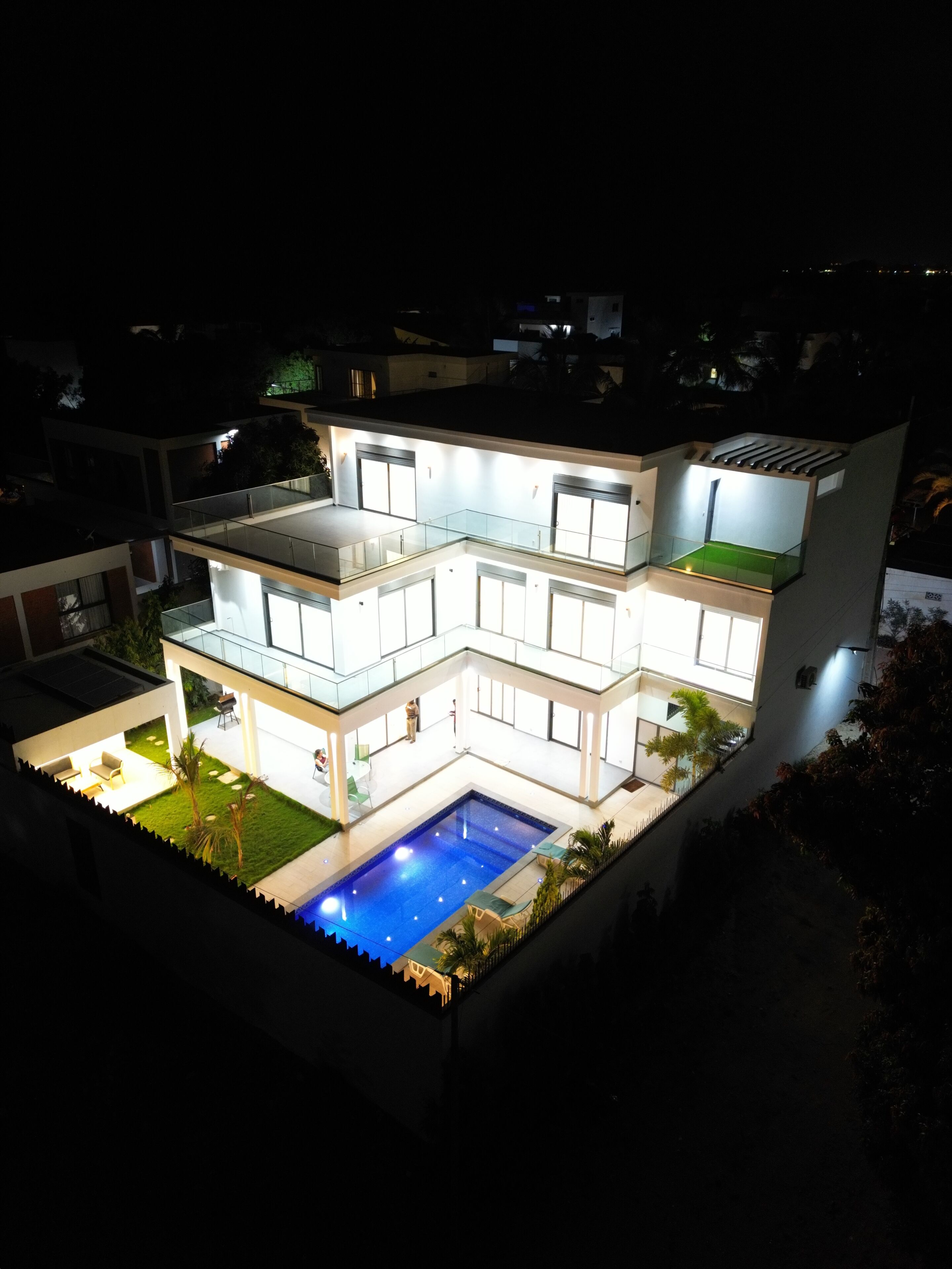 A modern multi-story house with a swimming pool, balconies, and a well-lit exterior.