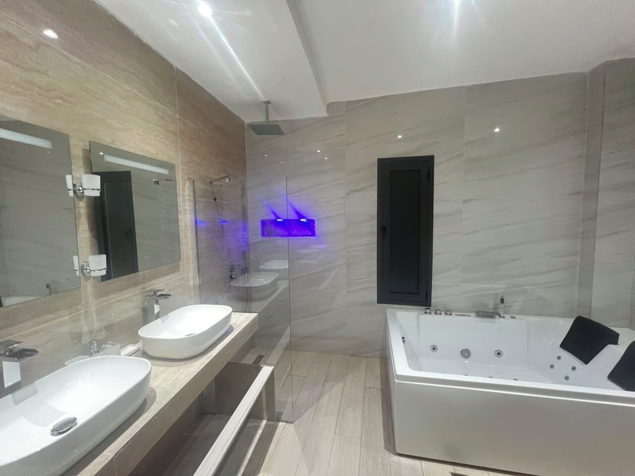 Ein modernes Badezimmer mit zwei Waschbecken, einer Badewanne und einer Duschkabine aus Glas.