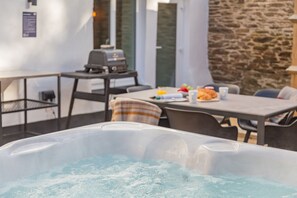 Un jacuzzi con una mesa y sillas cerca, una parrilla y una pared de piedra.