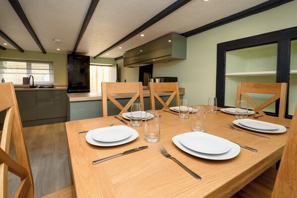 A dining area with a wooden table set for four, surrounded by wooden chairs. - Three-bedroom cottage with Wi-Fi, Netflix-ready TV, private decking, Ninja BBQ, EV charging and a hot tub, perfect for easy escapes. Up to three dogs are welcome too. (Cornwall)