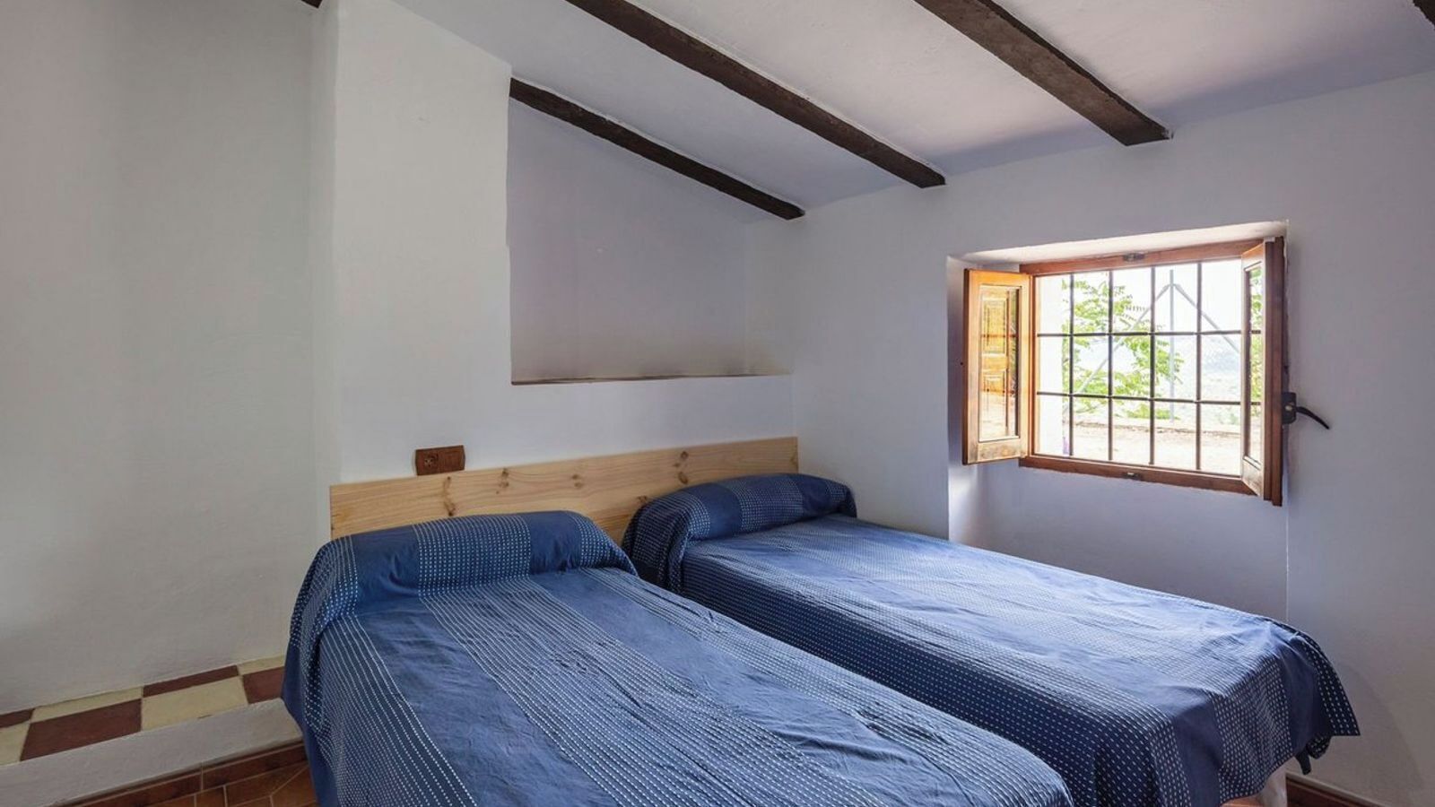 Une chambre avec deux lits, une fenêtre donnant sur un beau paysage et une poutre en bois au plafond.