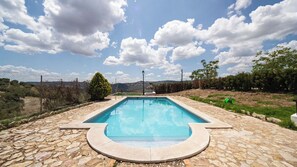 A rectangular swimming pool with a stone deck, surrounded by a fence and trees, under a partly cloudy sky. - El Ventorro Loja by Ruralidays (Granada)