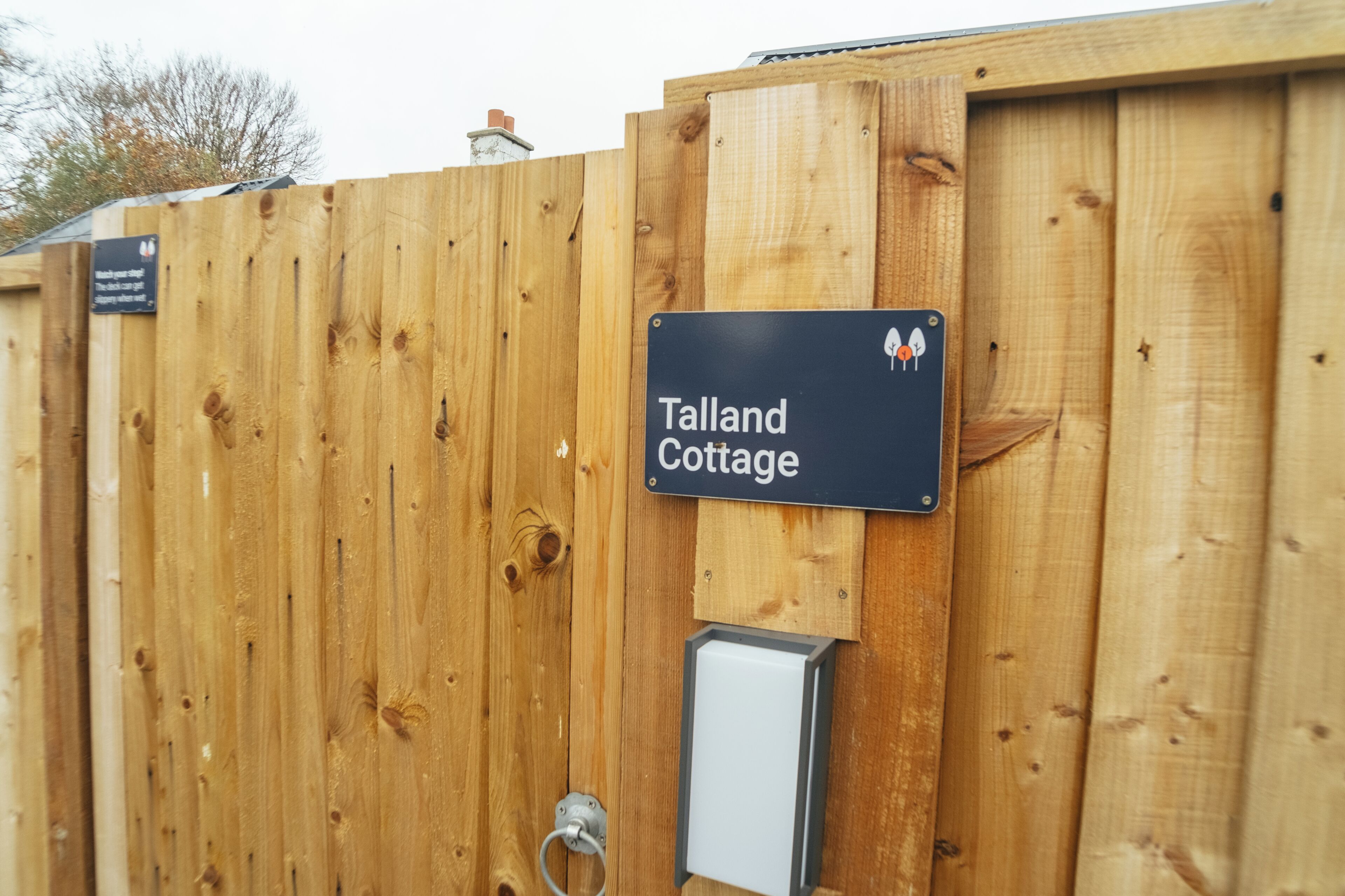 A wooden fence with a sign reading 'Talland Cottage.'