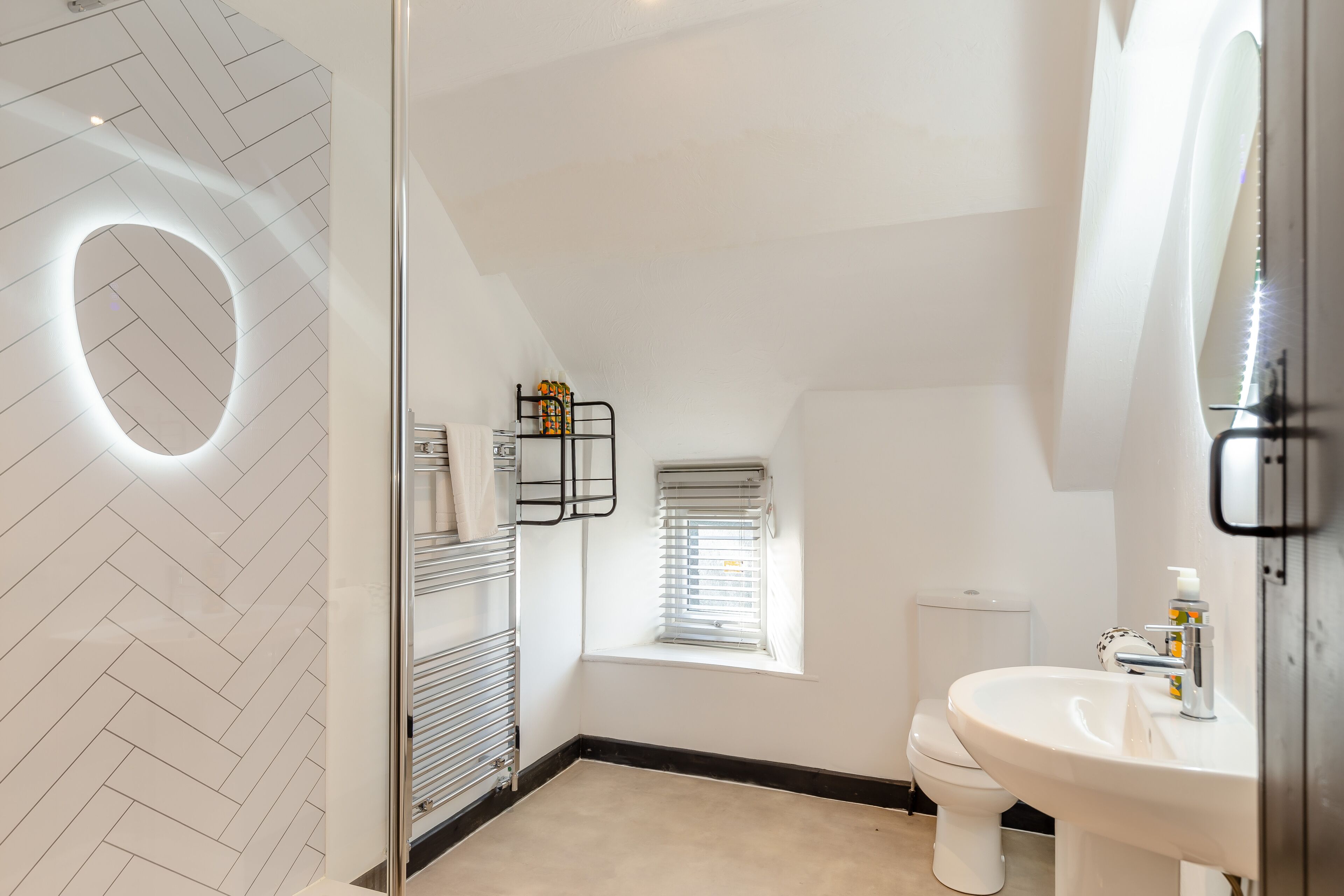 Ein modernes Badezimmer mit Fischgrätmuster bei den Fliesen, einer Glasdusche, einer Toilette und einem Waschbecken mit Spiegel.