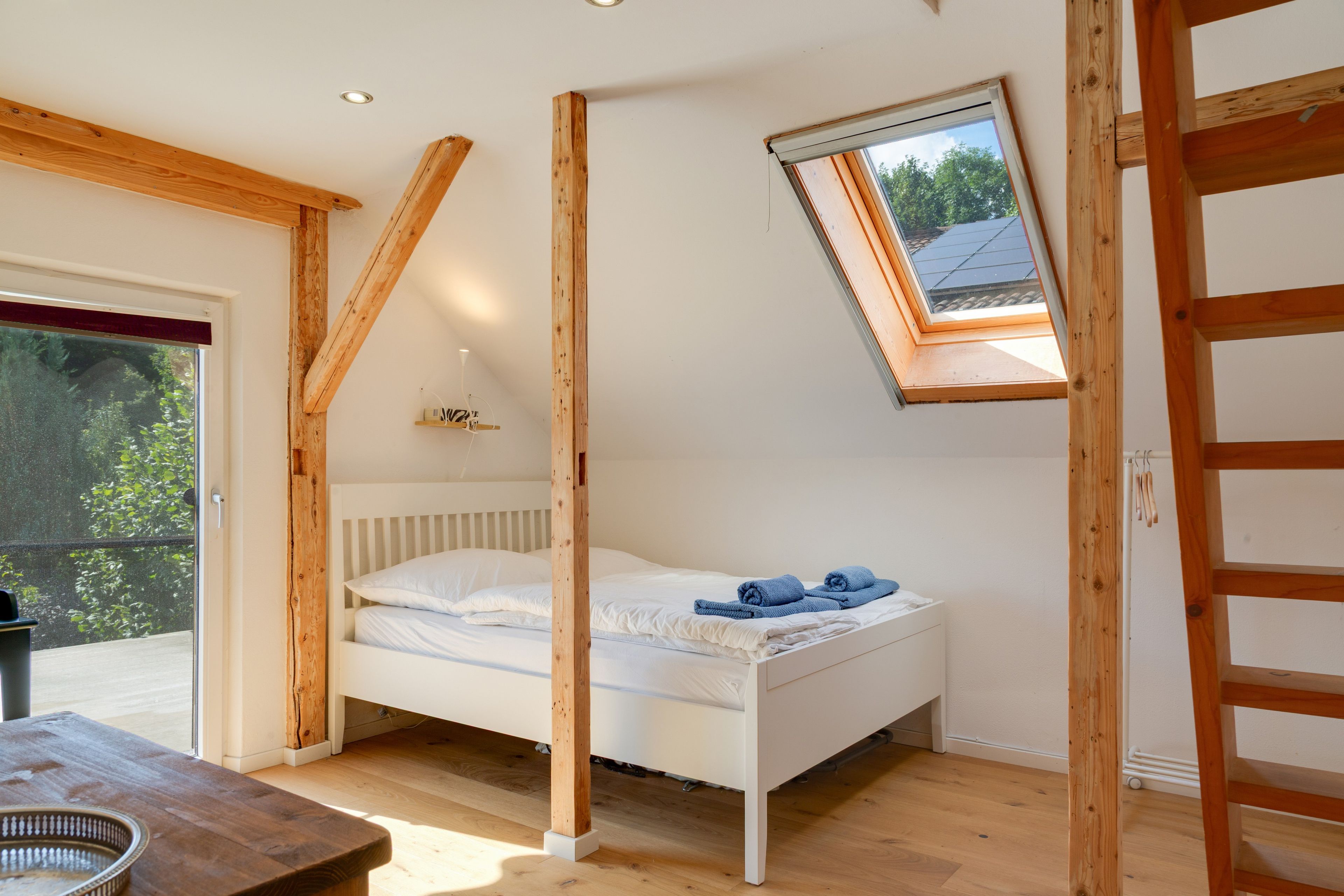 A bedroom with a sloped ceiling, a skylight, a bed, and a wooden table.