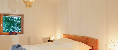A bedroom with a bed, a bedside table, a lamp, and a window with a view of trees.