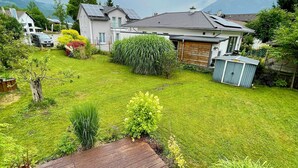 Un pati d'habitatge amb una terrassa de fusta, plantes en testos i una casa amb panells solars.