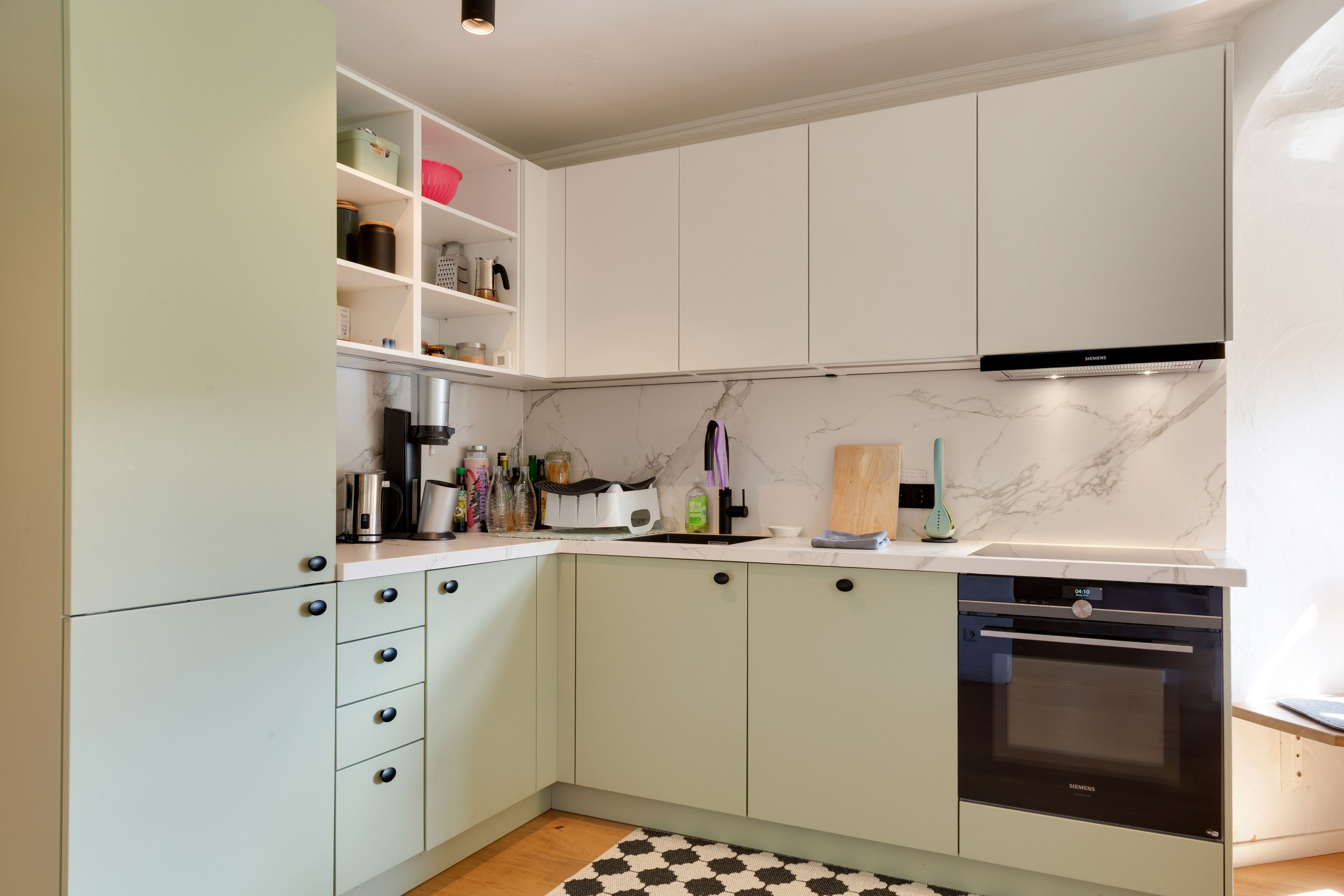 A modern kitchen with white cabinetry, a built-in oven, and a marble backsplash.