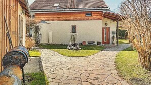 Una casa amb un camí de pedra que porta a l'entrada, un jardí petit amb una fonta i una tanca de fusta a l'esquerra.