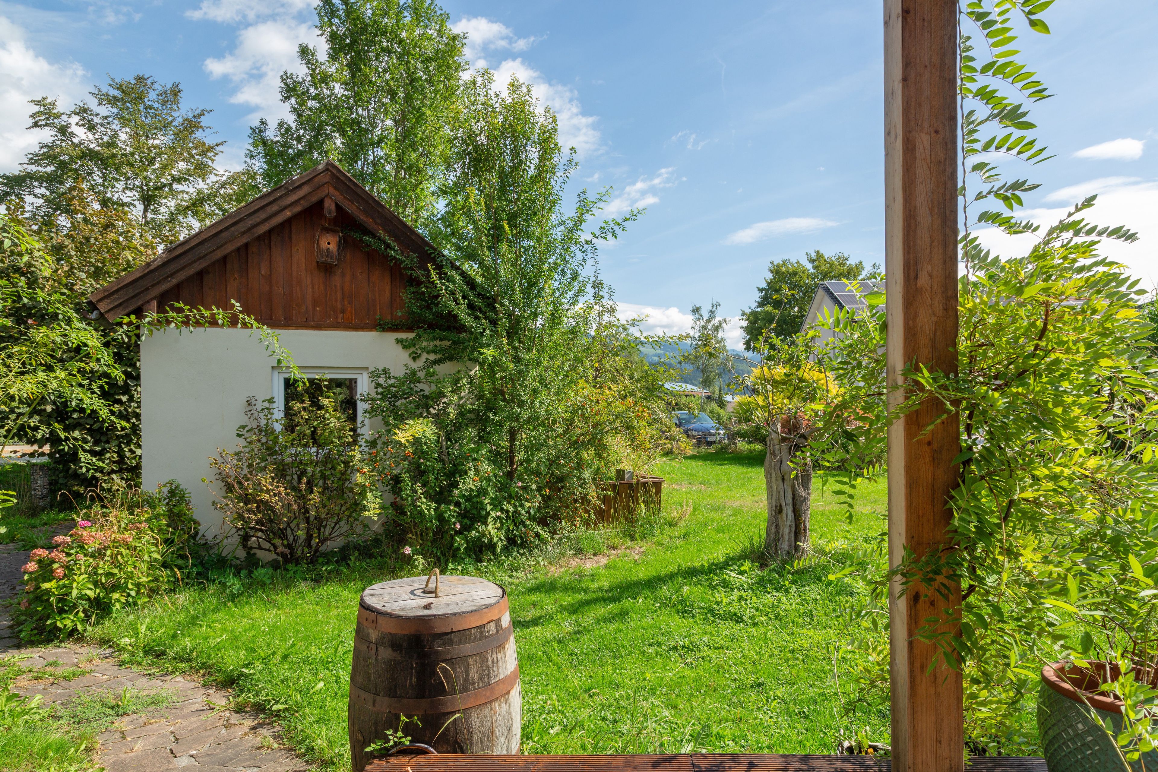 A rustic wooden house with a white exterior, surrounded by lush greenery and a clear sky.