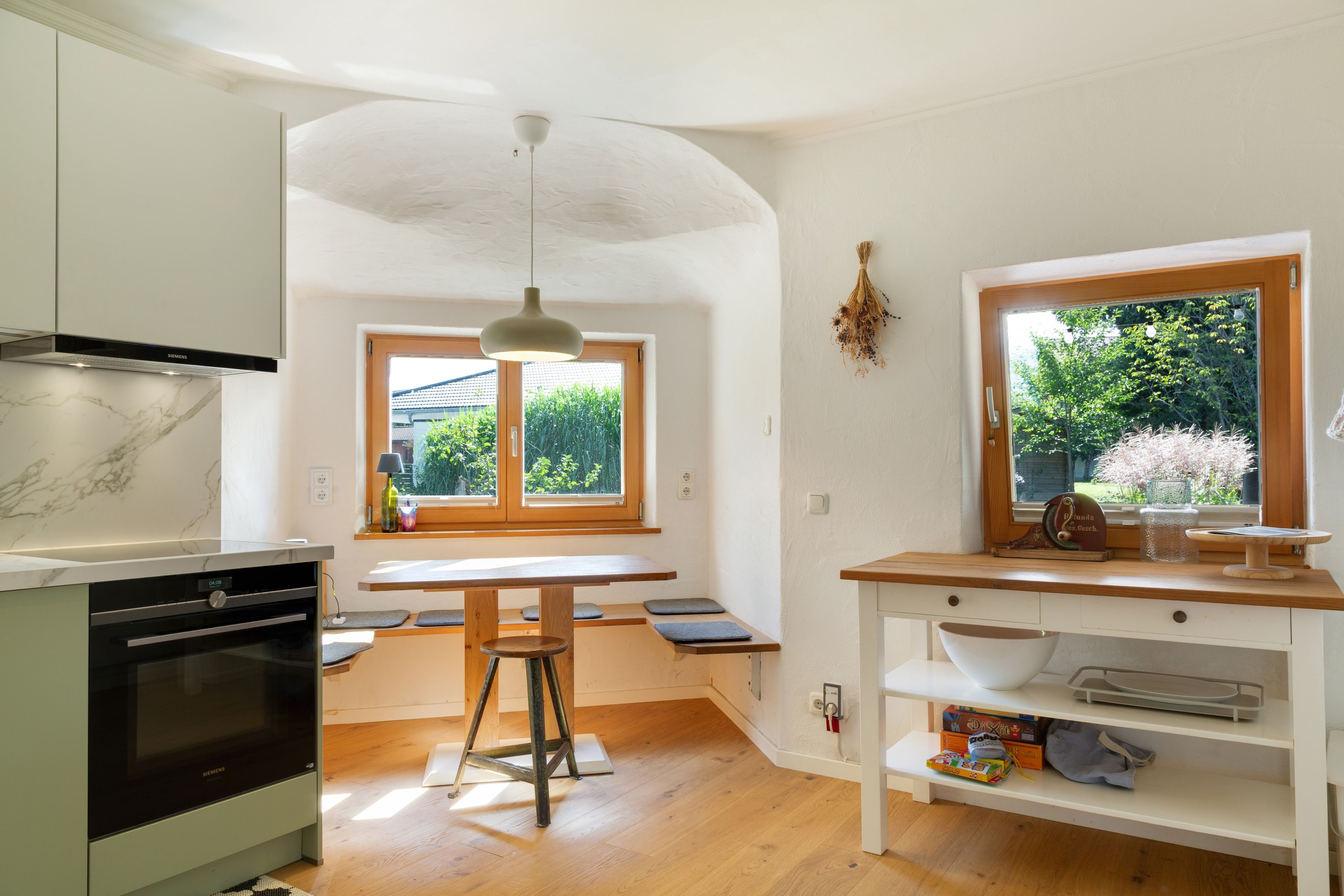 Cozinha moderna com forno embutido, mesa de jantar com bancos e janela com vista para o verde.