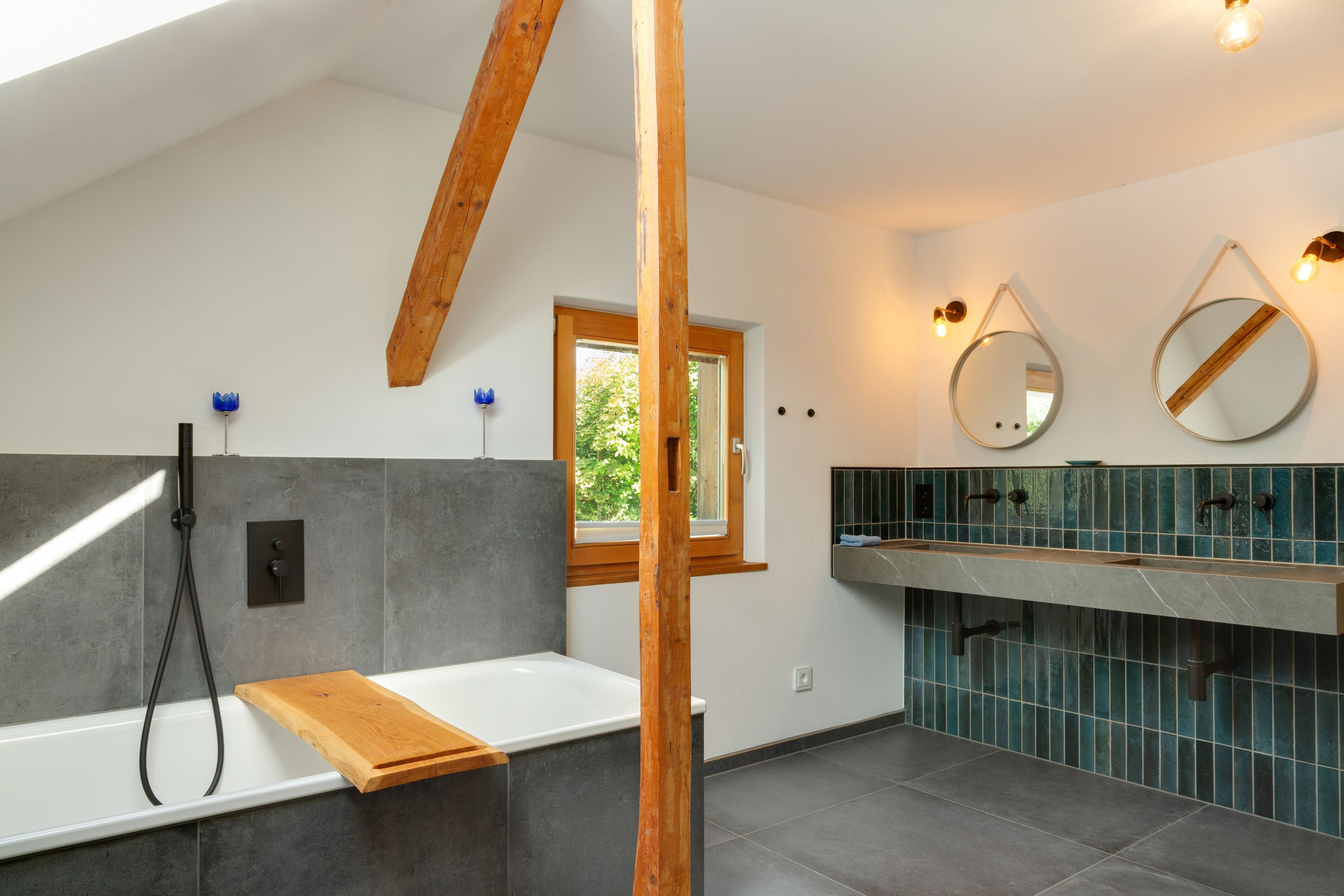 Ein modernes Badezimmer mit einer Badewanne, einer hölzernen Sitzbank, einem Fenster und einem Waschtisch mit Spiegel.