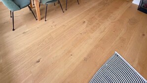 Una zona de menjador amb taula de fusta, cadires grises i lluminàries penjants.