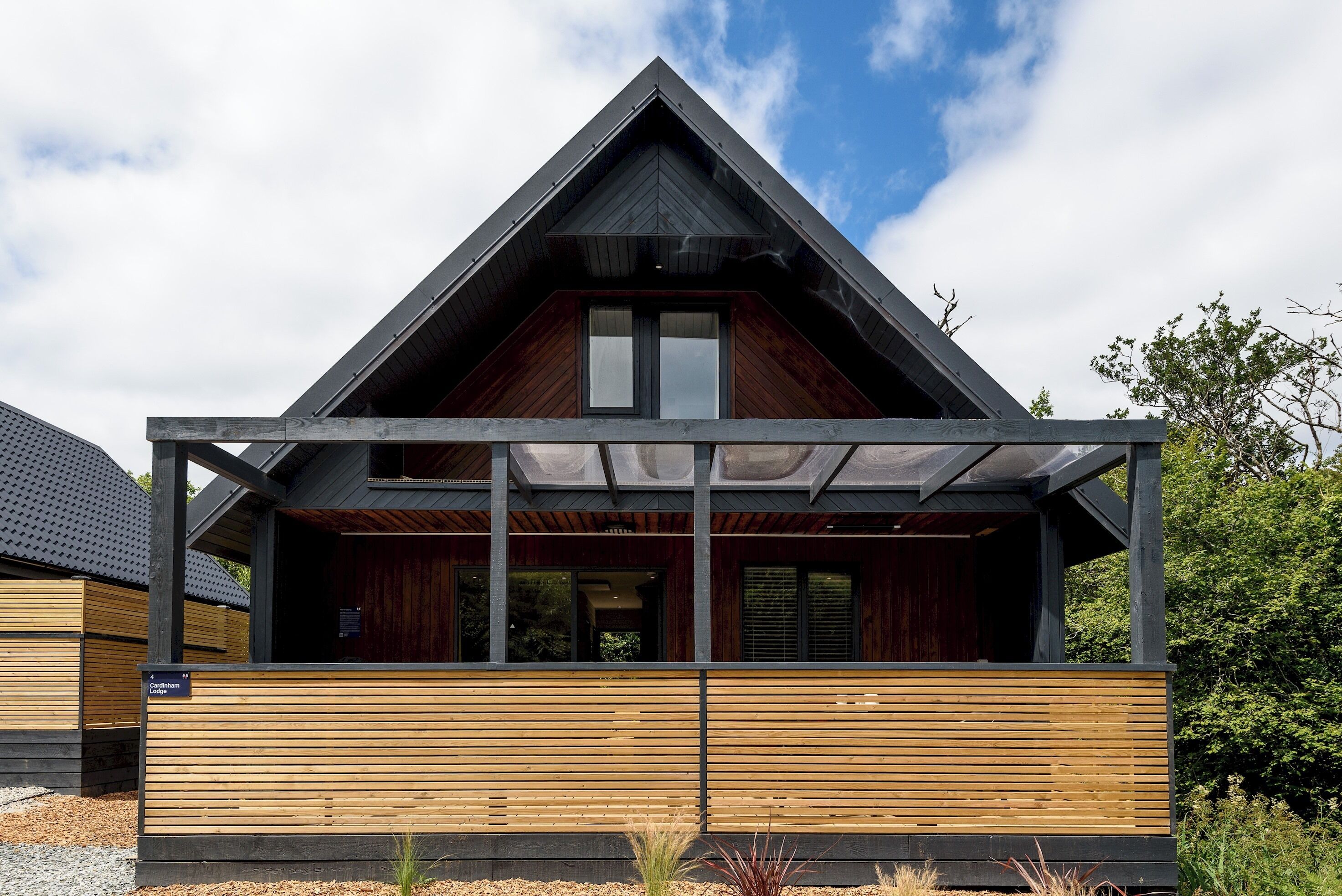 Una casa moderna con techo inclinado, fachada de madera y un porche cubierto.