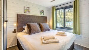 Une chambre d’hôtel moderne avec un grand lit, deux tableaux accrochés au mur, une fenêtre avec des rideaux et une porte bien visible.