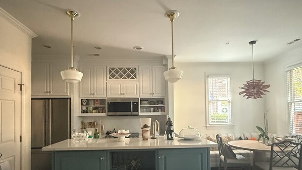 A kitchen with white cabinets, a blue island, pendant lights, and a dining area with a table and chairs. - Beautiful designer home located near SouthEnd, LoSo, Rail and Uptown (Charlotte)