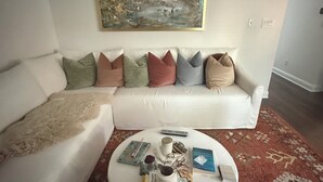 A living room with a white sofa set, a coffee table with books and decorative items, and a painting on the wall. - Beautiful designer home located near SouthEnd, LoSo, Rail and Uptown (Charlotte)