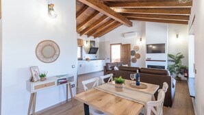 Ein modernes Interieur mit einem Holztisch, weißen Stühlen, einem braunen Sofa und einer Küche im Hintergrund.