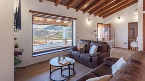 Ein Wohnzimmer mit einem großen Fenster, einem braunen Ledersofa, einem kleinen runden Tisch und einer Holzzieldecke.