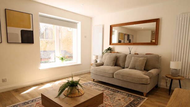 Un salon avec un canapé, une table basse, un miroir et une fenêtre avec des stores.