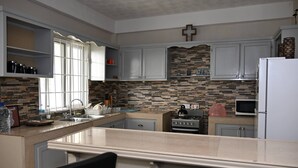 A kitchen with a stone backsplash, a stove, a microwave, and a cross on the wall. - Spacious 2BR Apartment in Cap Estate, Saint Lucia - Walk to Beaches (Gros Islet)