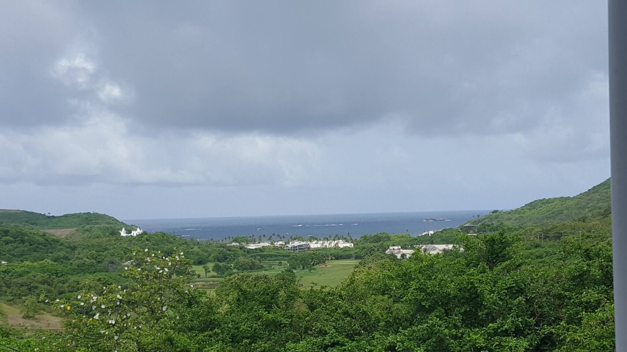 A coastal landscape with lush greenery, a view of the sea, and buildings in the distance.