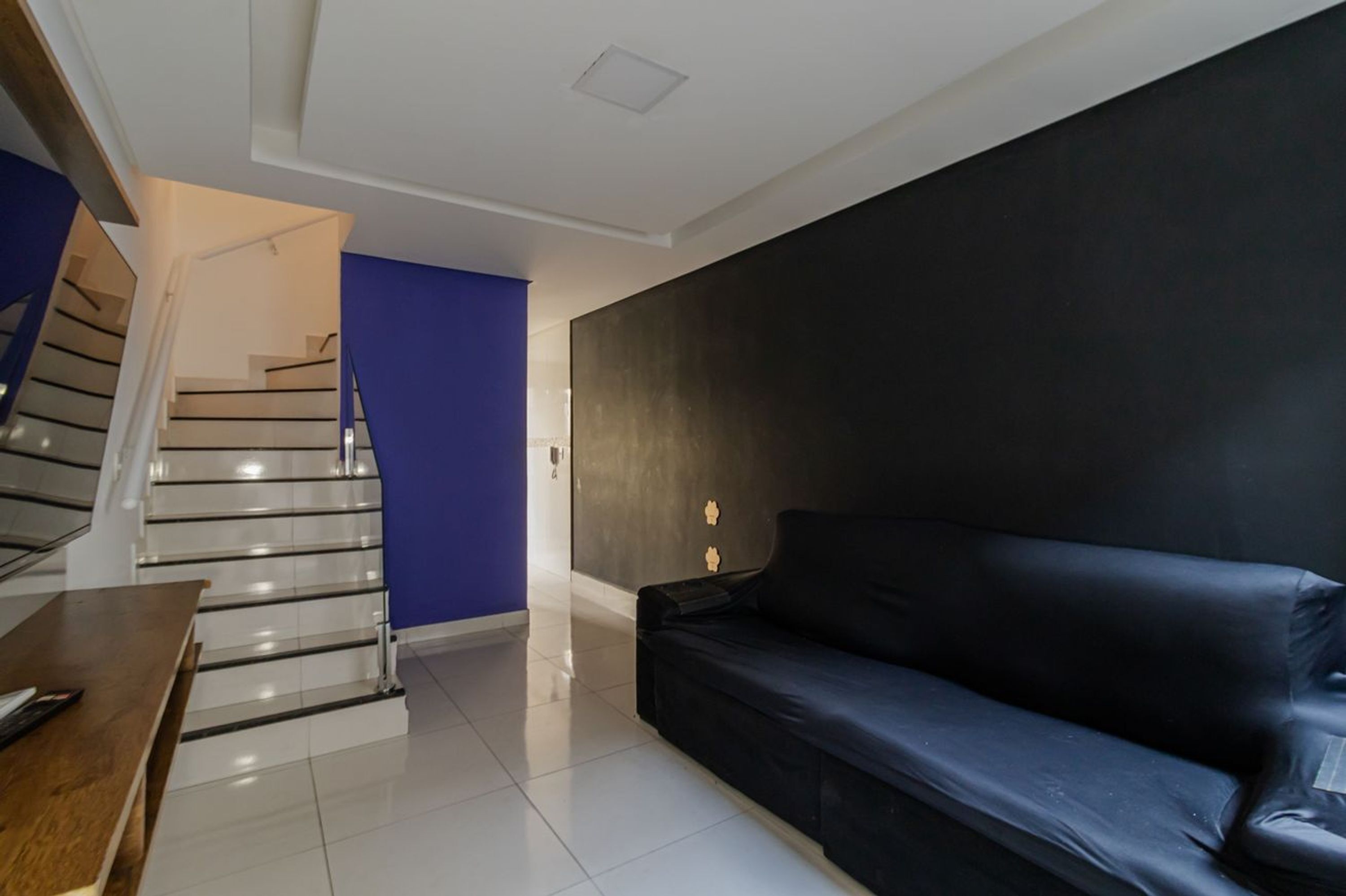 Ein modernes Wohnzimmer mit Treppe, einem schwarzen Ledersofa und einer blauen Akzentwand.