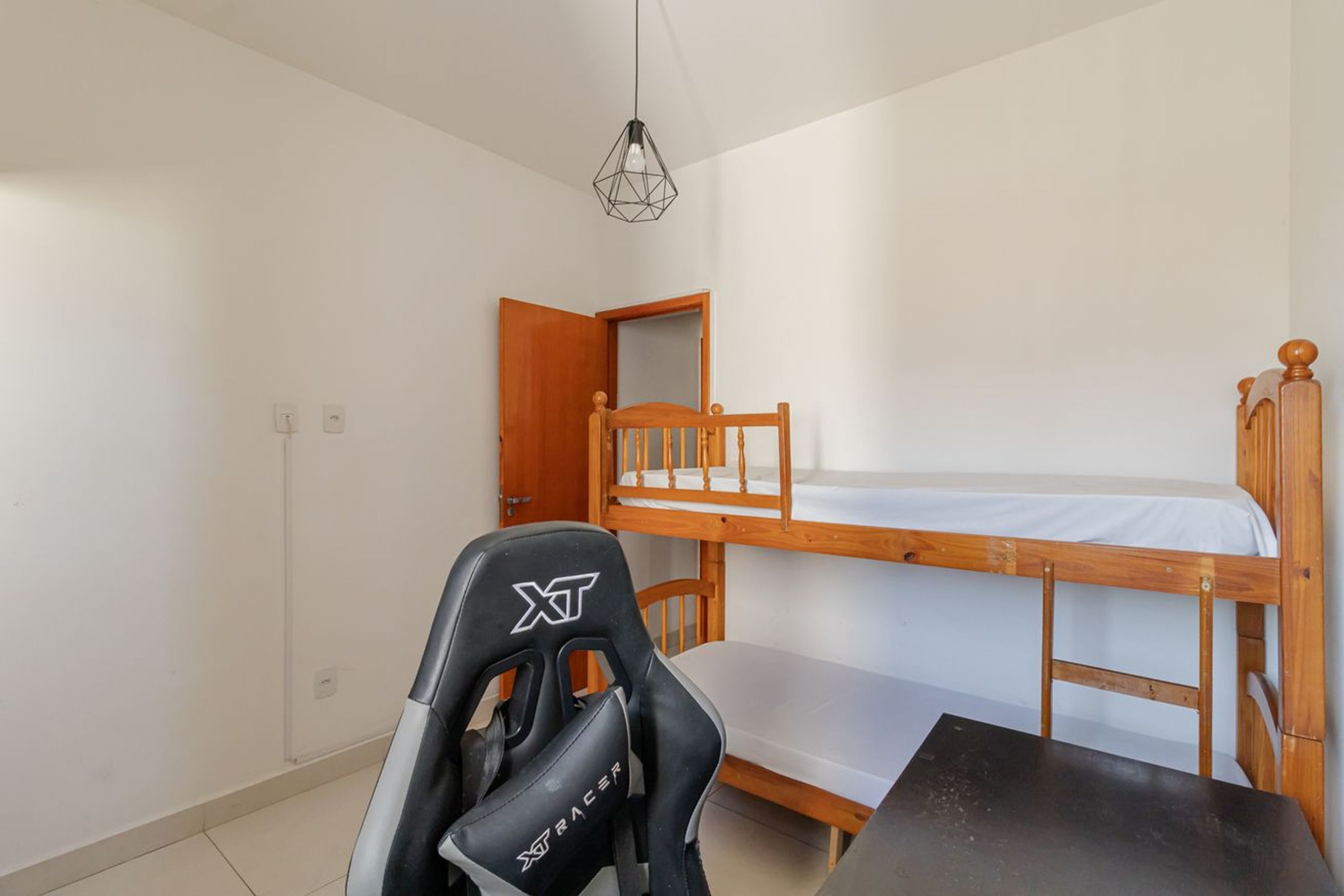 A single room with a bunk bed, a desk, a chair, and a hanging light fixture.