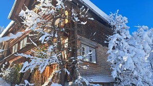 Una cabaña de madera con techo inclinado, rodeada de árboles cubiertos de nieve.