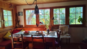 Un comedor de madera con una mesa, sillas, un florero con flores y una lámpara colgante.