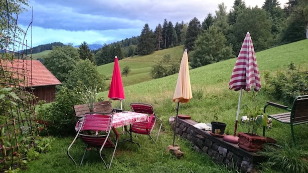 Un espacio al aire libre con mesa y sillas, dos sombrillas y un muro de piedra.