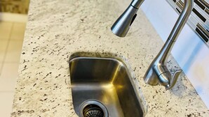 Een keuken met een RVS spoelbak, een kraan en een granieten aanrecht.