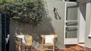Een terras met twee rieten stoelen, een wandlamp en een schuifdeur met glas.