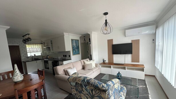 Een moderne woonkamer met een bank, een fauteuil met een patroon, een eettafel en een keuken op de achtergrond.