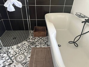 A bathroom with a bathtub, black and white patterned tiles, a brown towel, and a wicker basket. - Rosarios Village 2-bed Unit 01, Bryanston (Johannesburg)