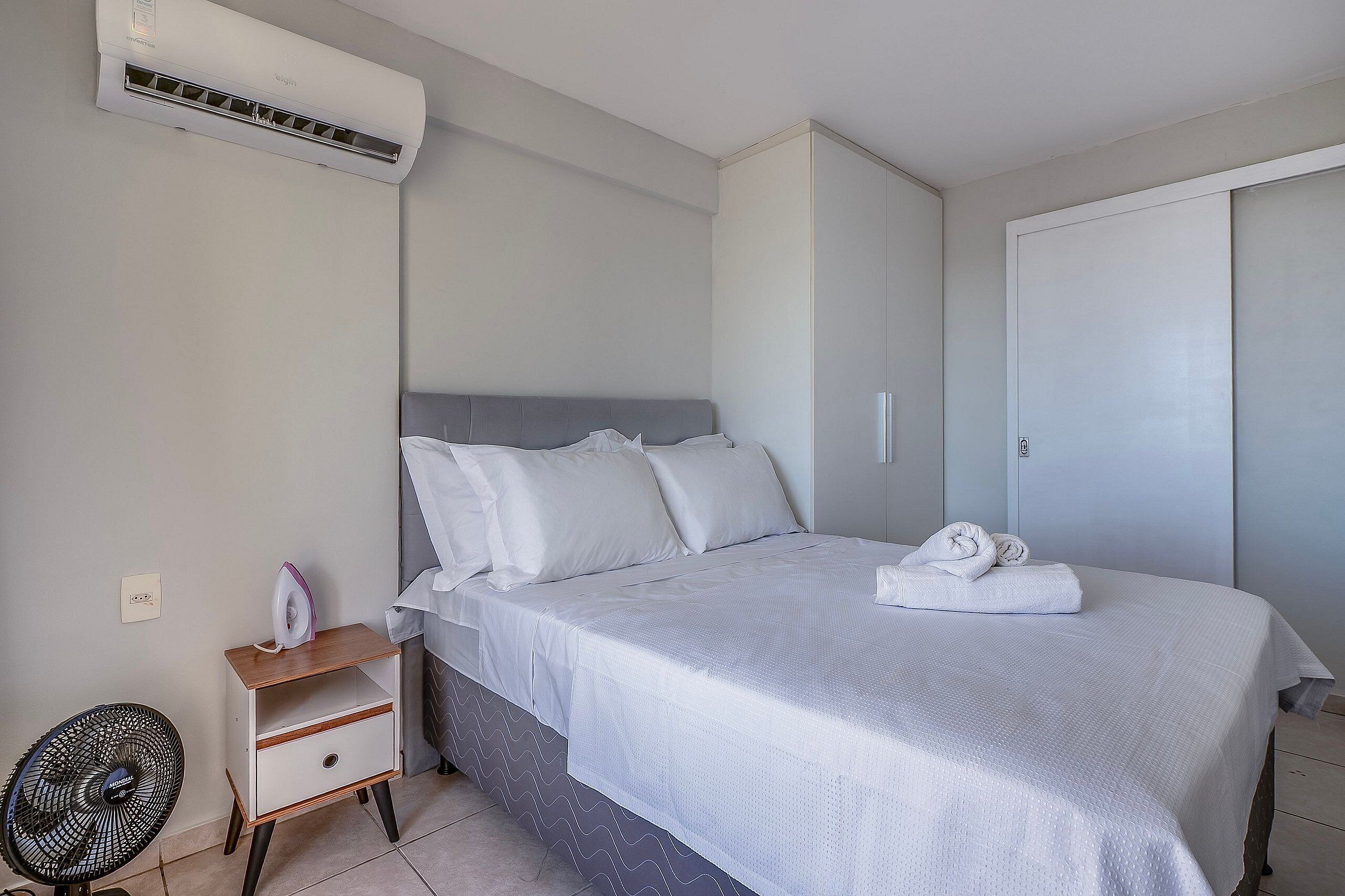 Un dormitorio con cama, mesita de noche, aire acondicionado, ventilador y armario.