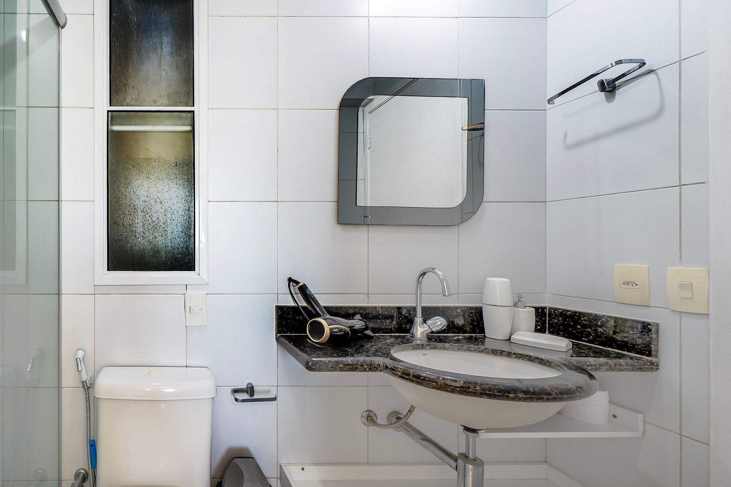 A bathroom with a white toilet, a sink with a marble countertop, a mirror, and a towel rack.