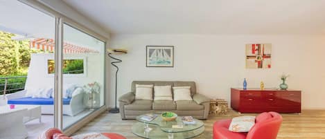 En stue med et glas sofabord, røde lædersofaer, en beige sofa, et rødt skab og et maleri af en sejlbåd på væggen.